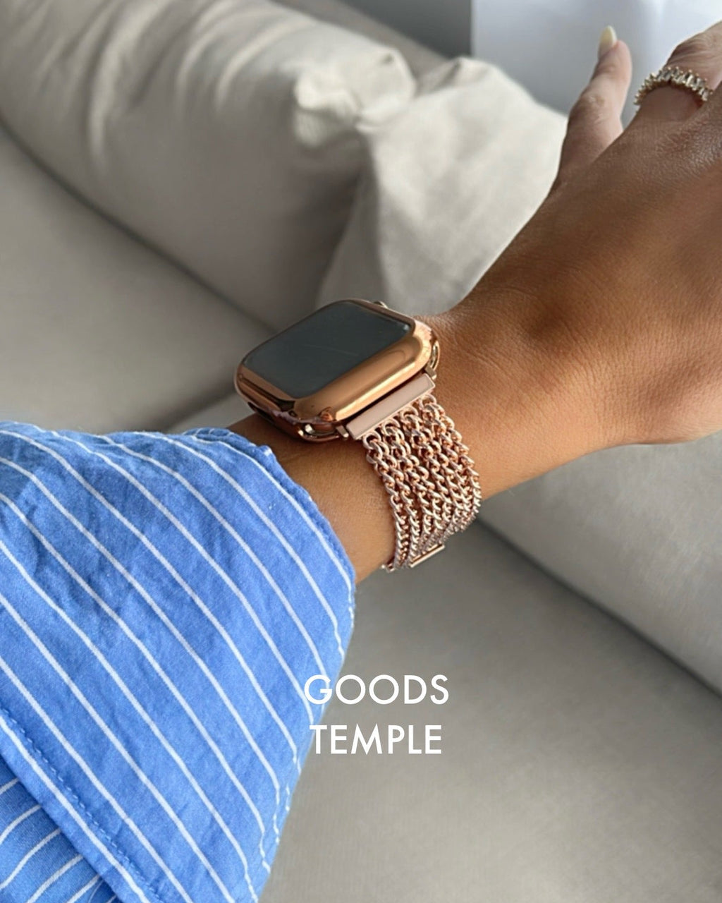 Person wearing a smartwatch with a rose gold band on a light-colored couch.
