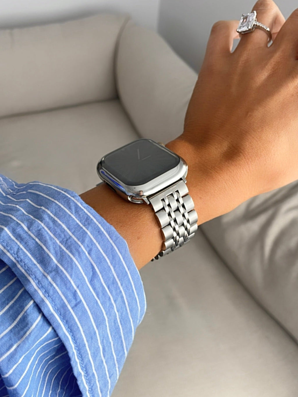 Person wearing a silver smartwatch on a light-colored couch