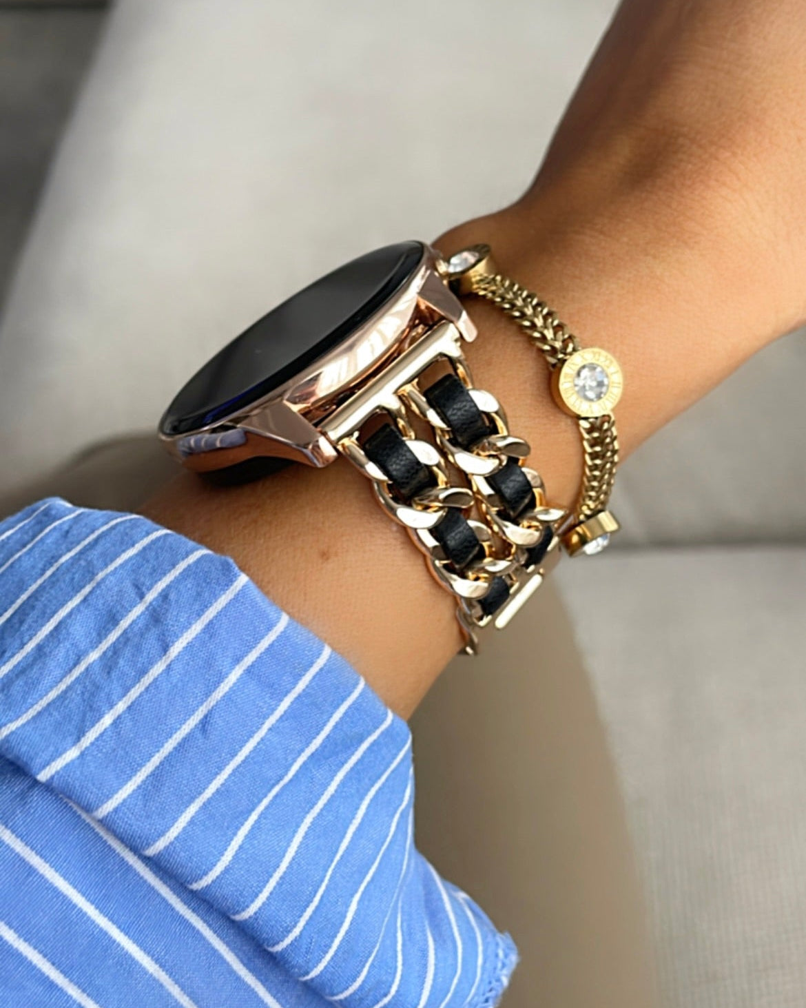 Close-up of a wrist wearing a gold watch and bracelet on a neutral background
