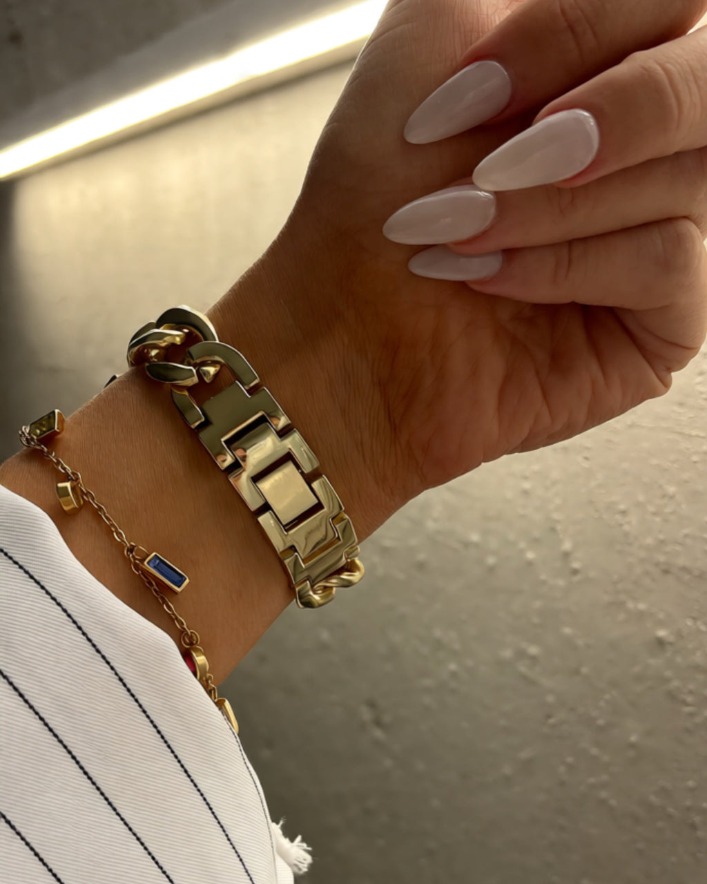 Hand wearing gold bracelets with a neutral background