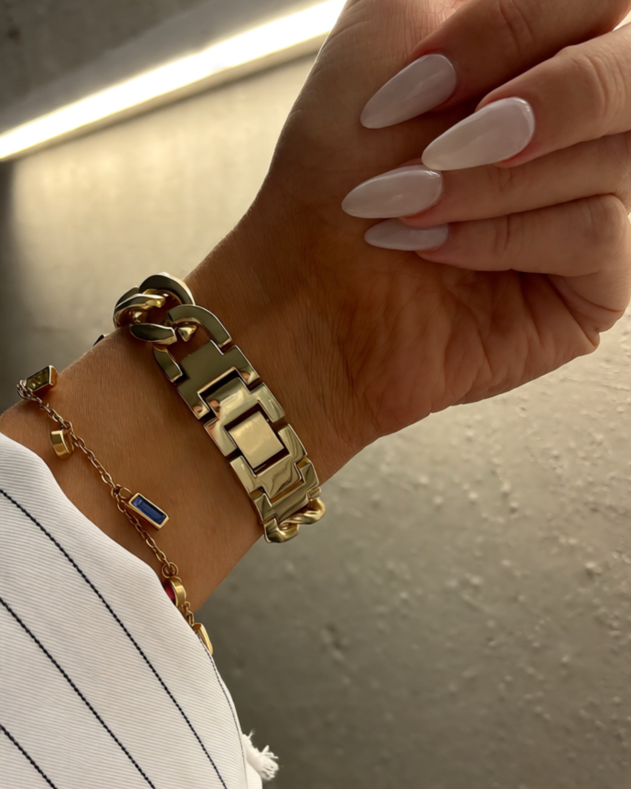 Hand wearing gold bracelets with a neutral background