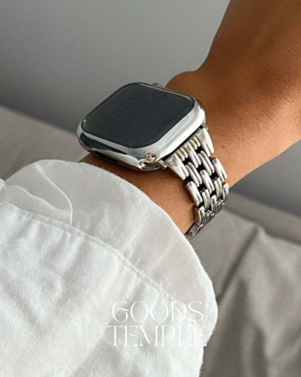 Smartwatch with a metal band on a wrist, wearing a white shirt.