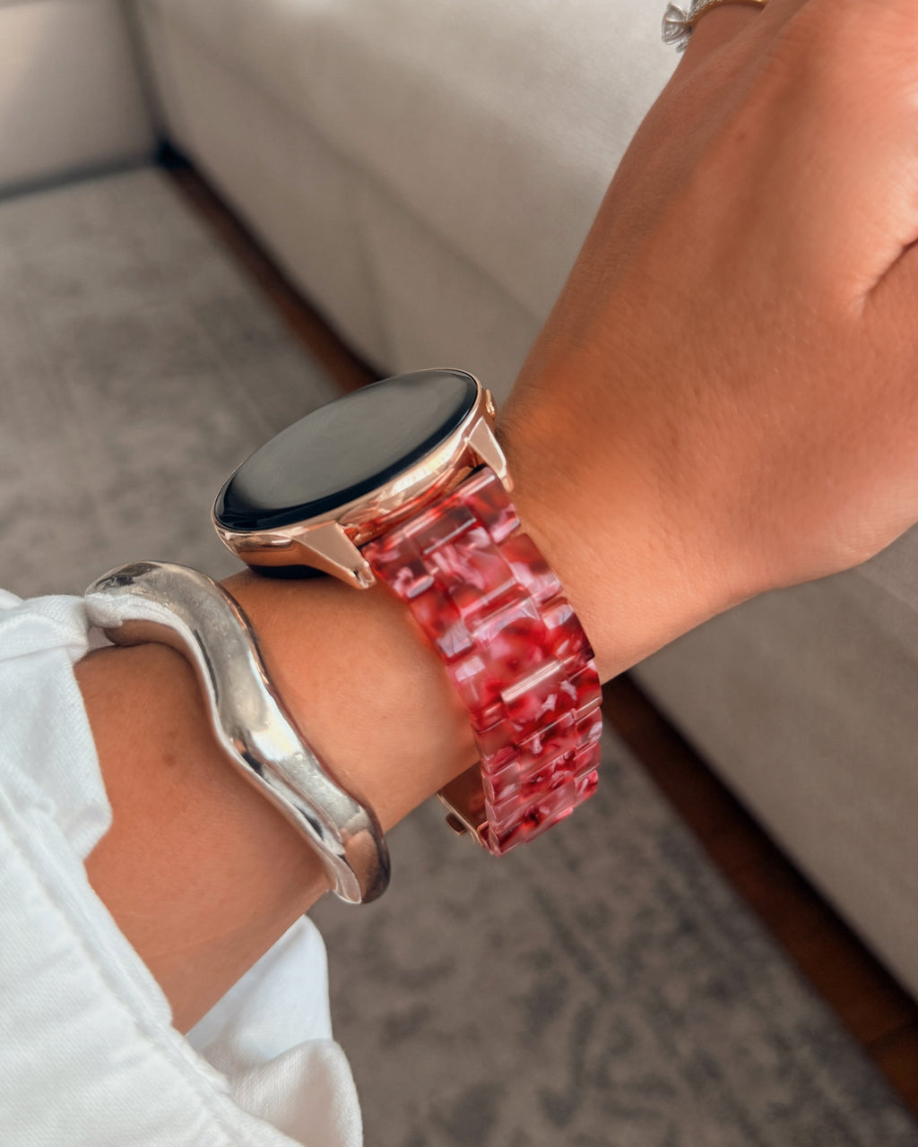 Person wearing a smartwatch with a red marble band in a casual setting.