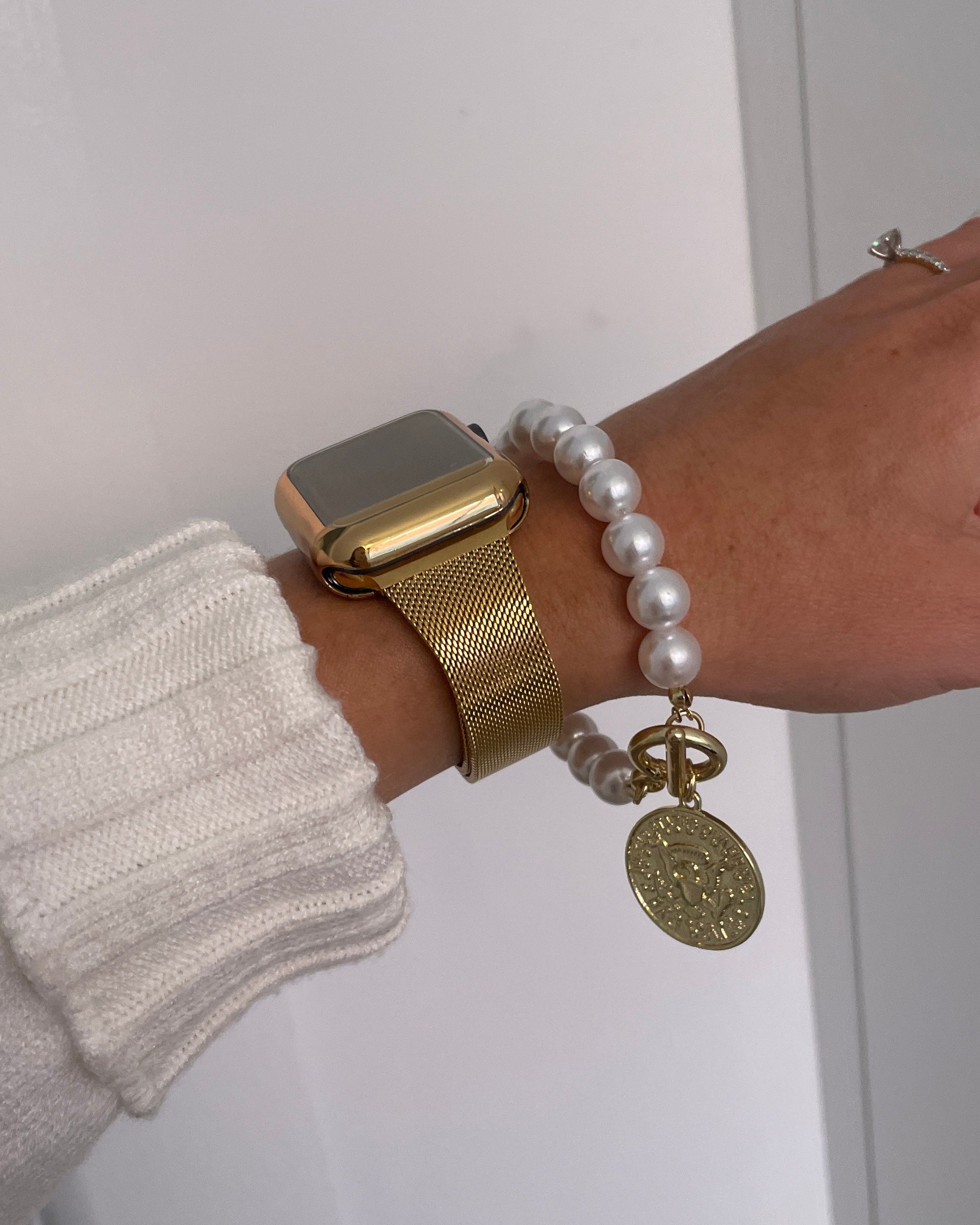 Gold watch and pearl bracelet with gold charm on a wrist against a white background