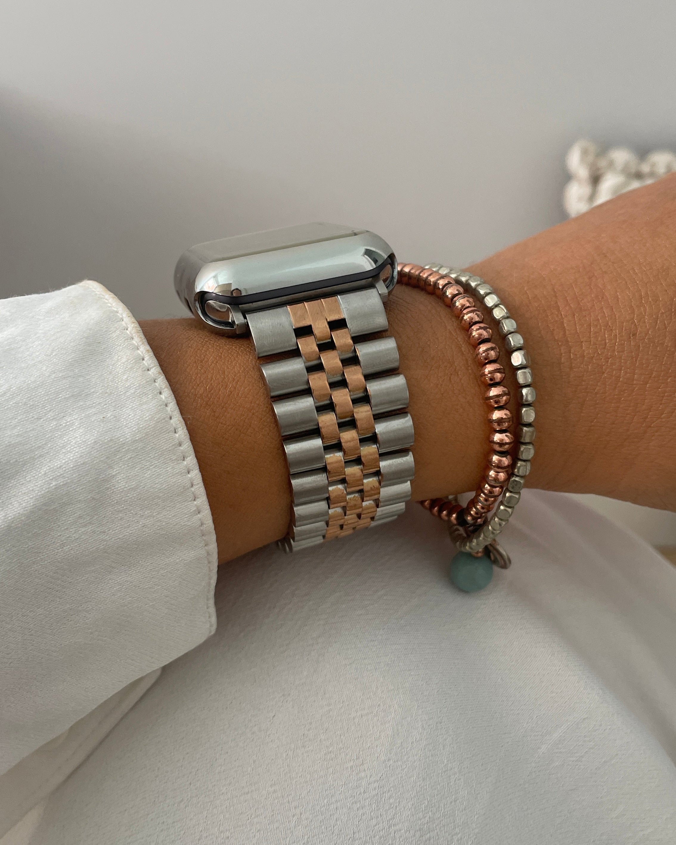 Close-up of a wrist wearing a silver watch and multiple bracelets on a white background