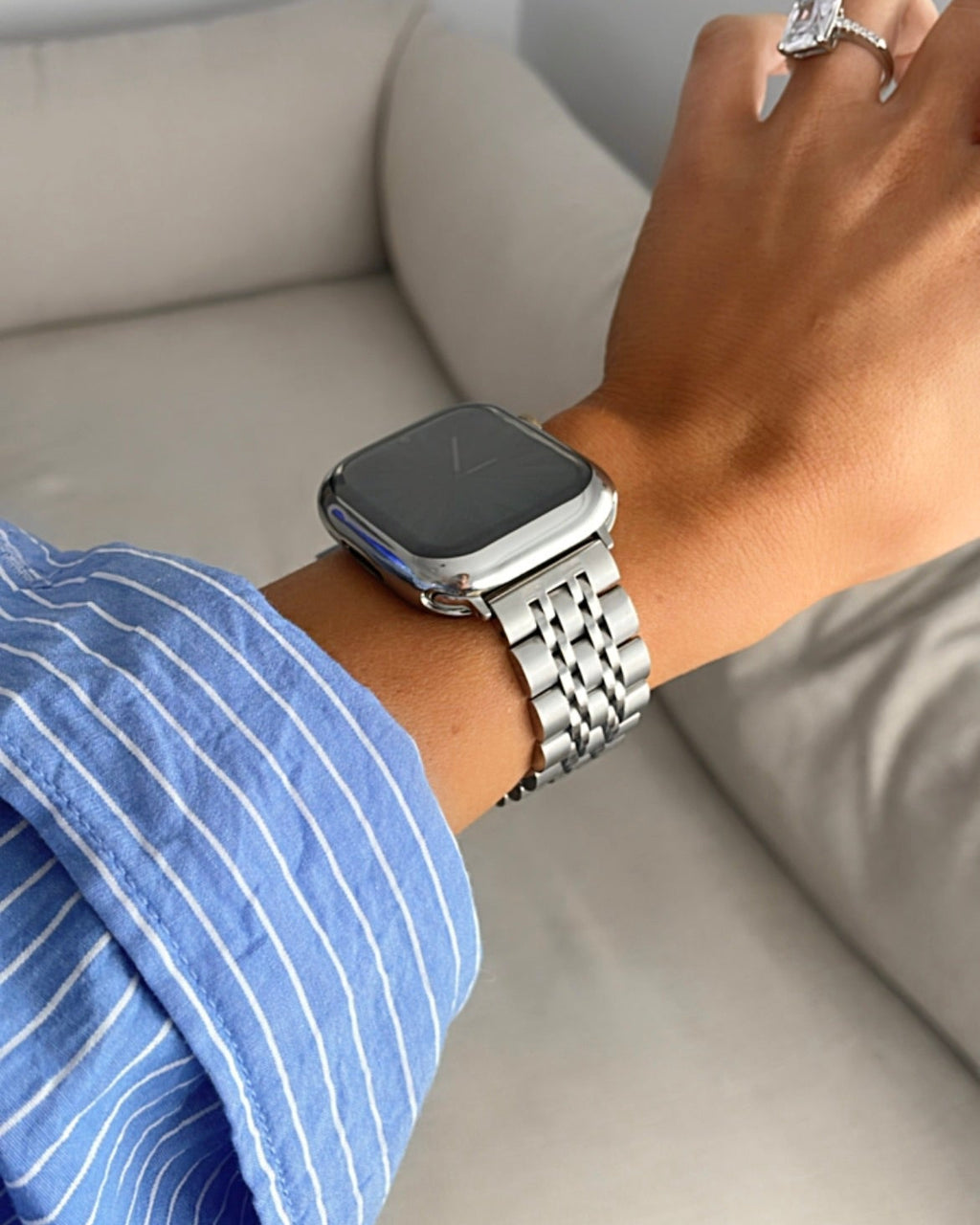 Person wearing a silver smartwatch on a light-colored couch