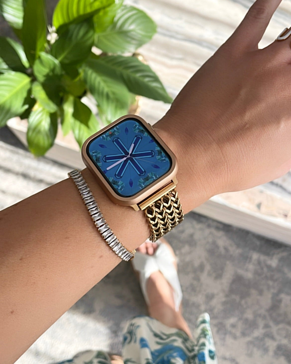 Person wearing a gold watch with a blue screen on a blurred outdoor background