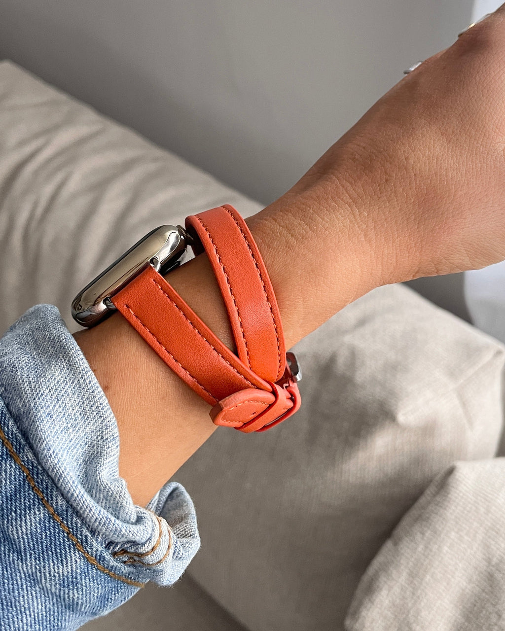 Person wearing an orange leather bracelet on a neutral background