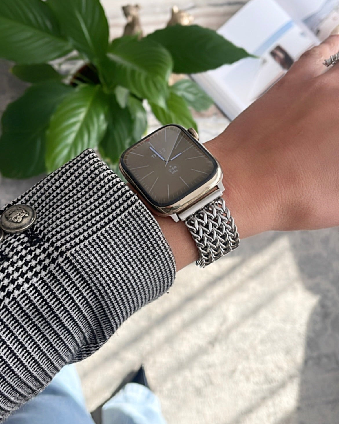 Person wearing a smartwatch with a mesh band, sitting on a stone surface with greenery in the background.