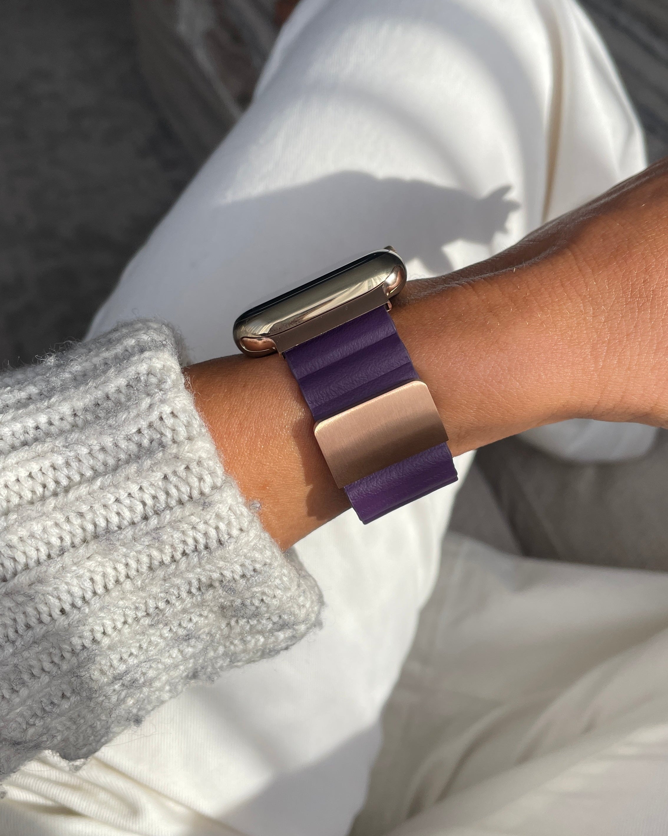 Person wearing a smartwatch with a purple band on a blurred indoor background