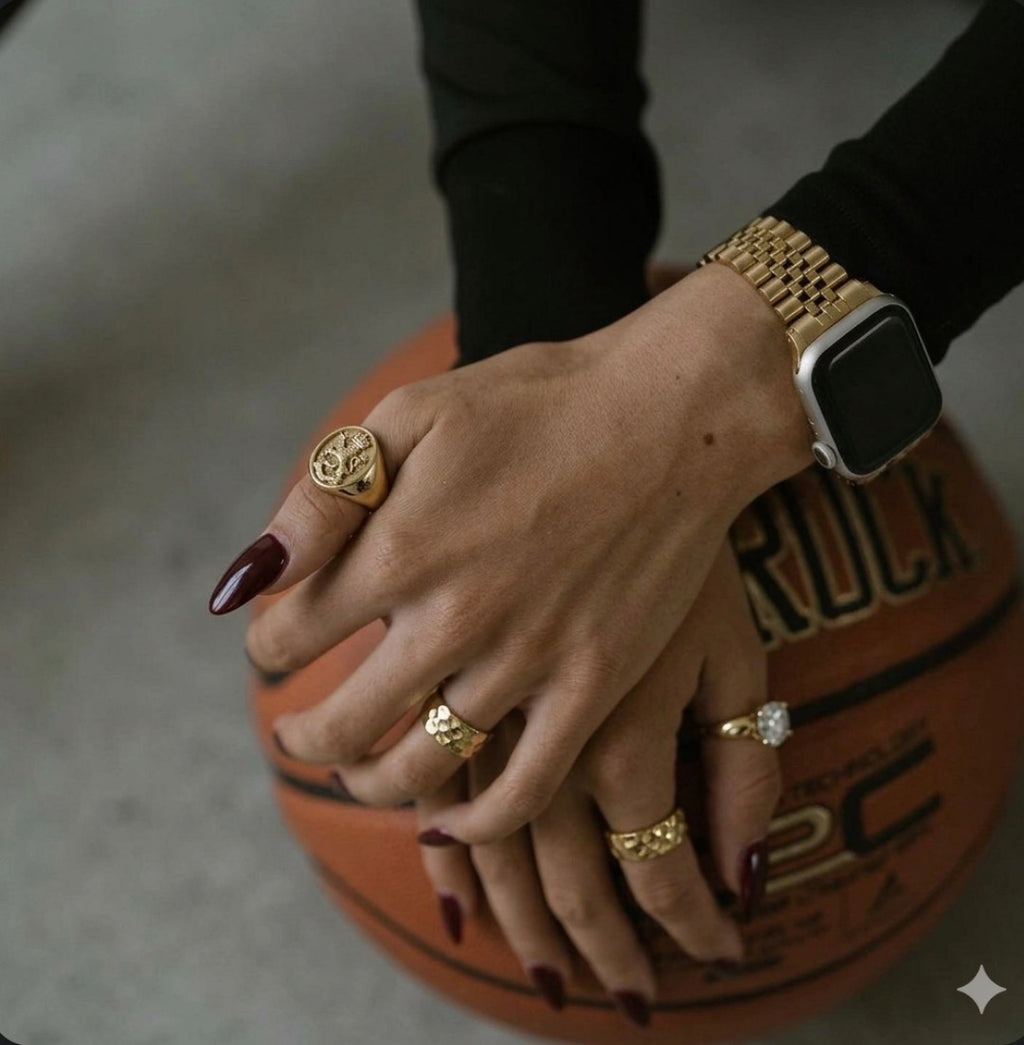 Hand with multiple gold rings holding a basketball, wearing a gold watch.
