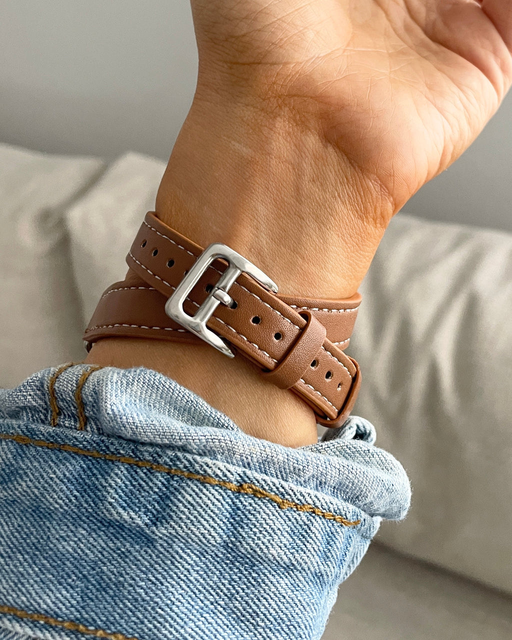 Brown leather bracelet with silver buckle on a wrist, wearing light blue jeans.