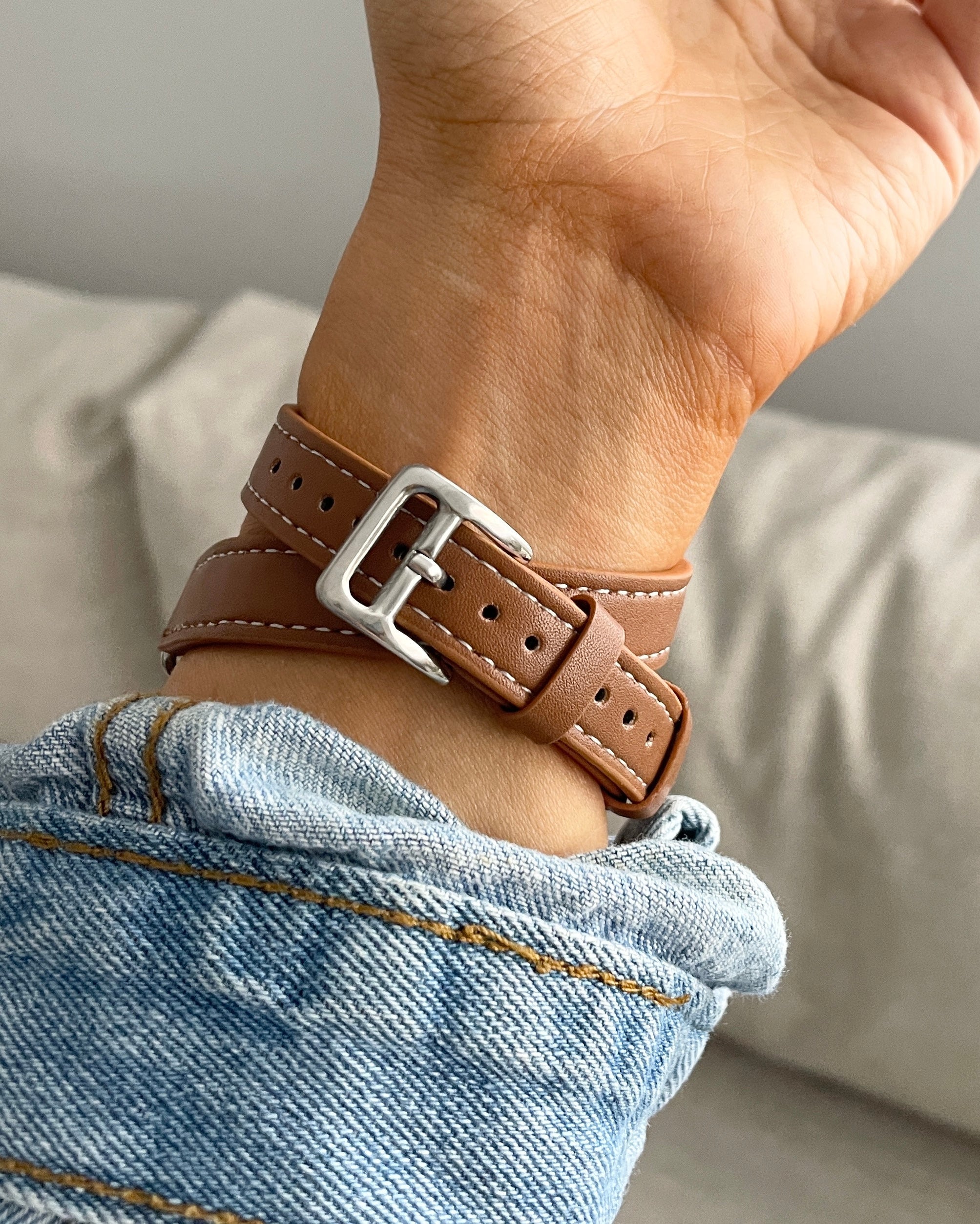 Brown leather bracelet with silver buckle on a wrist, wearing light blue jeans.