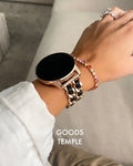 Hand wearing a smartwatch and bracelets with 'GOODS TEMPLE' branding.