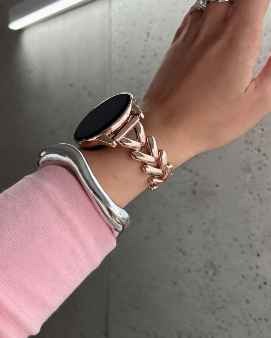 Hand wearing a silver bracelet with a pink sleeve against a neutral background