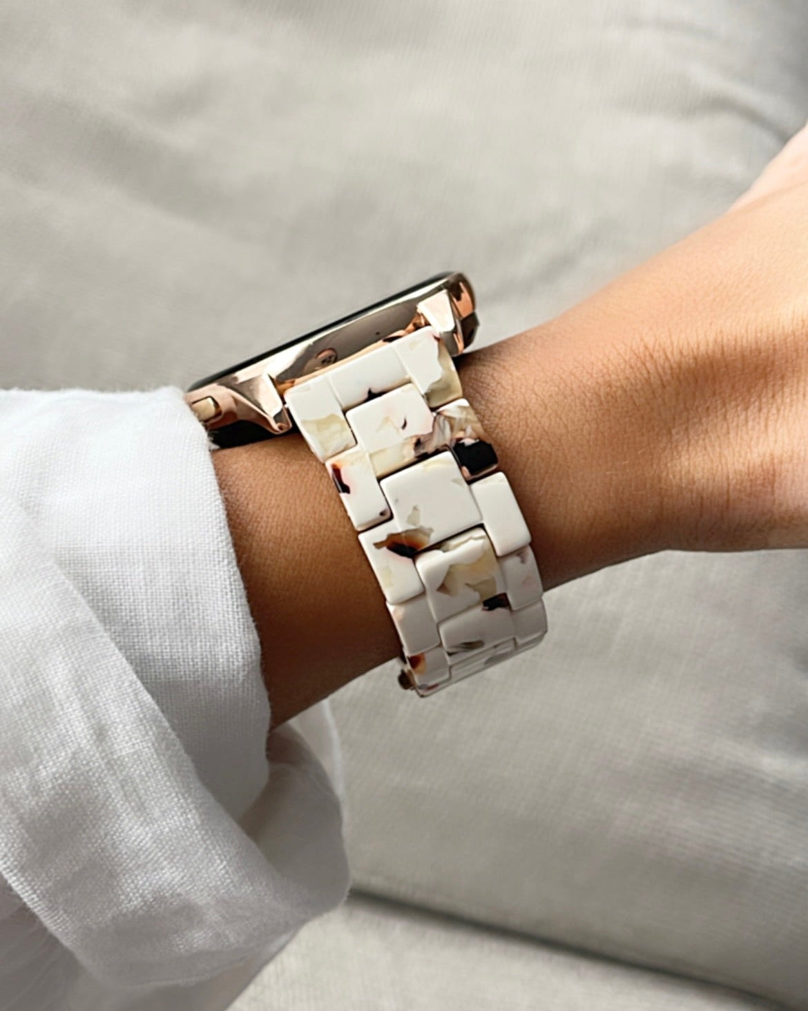 Close-up of a wrist wearing a rose gold and white ceramic bracelet on a light background