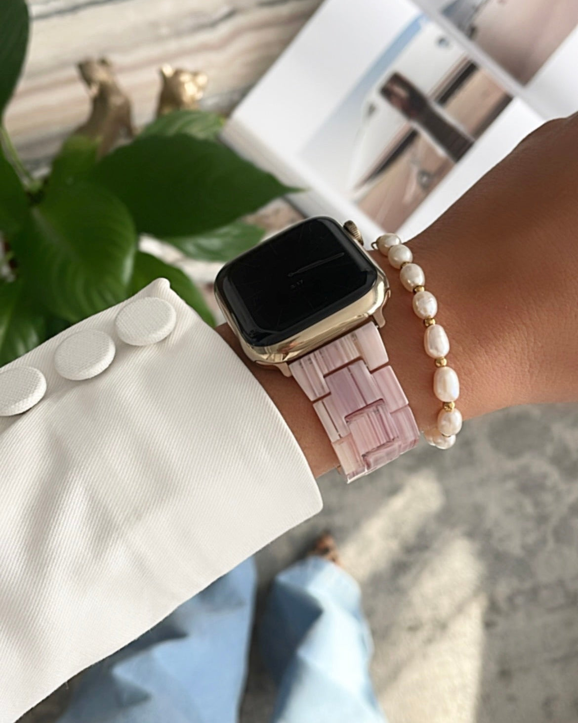 Person wearing a smartwatch with a pink band and pearl bracelet, standing outdoors.
