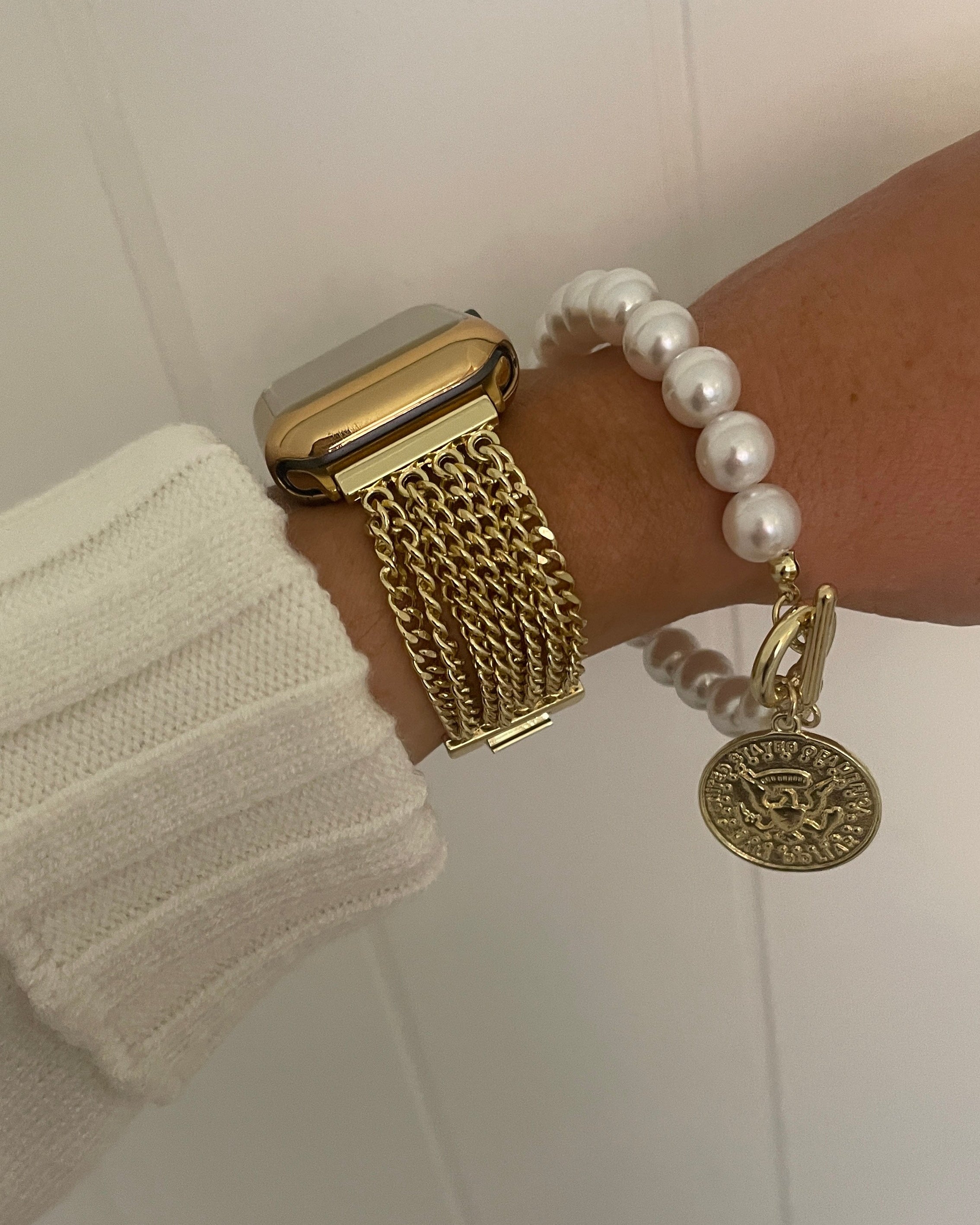 Gold watch and bracelet on a wrist against a white background