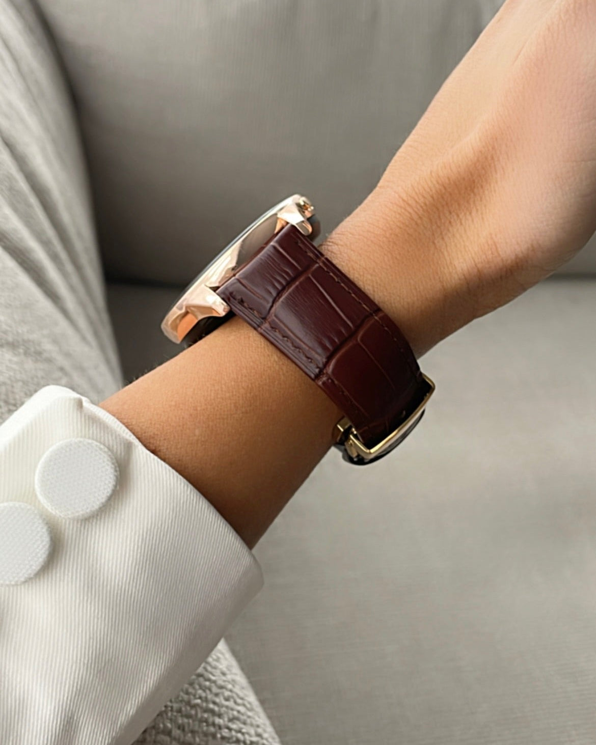 Close-up of a wrist wearing a brown leather watch with a white cuff background