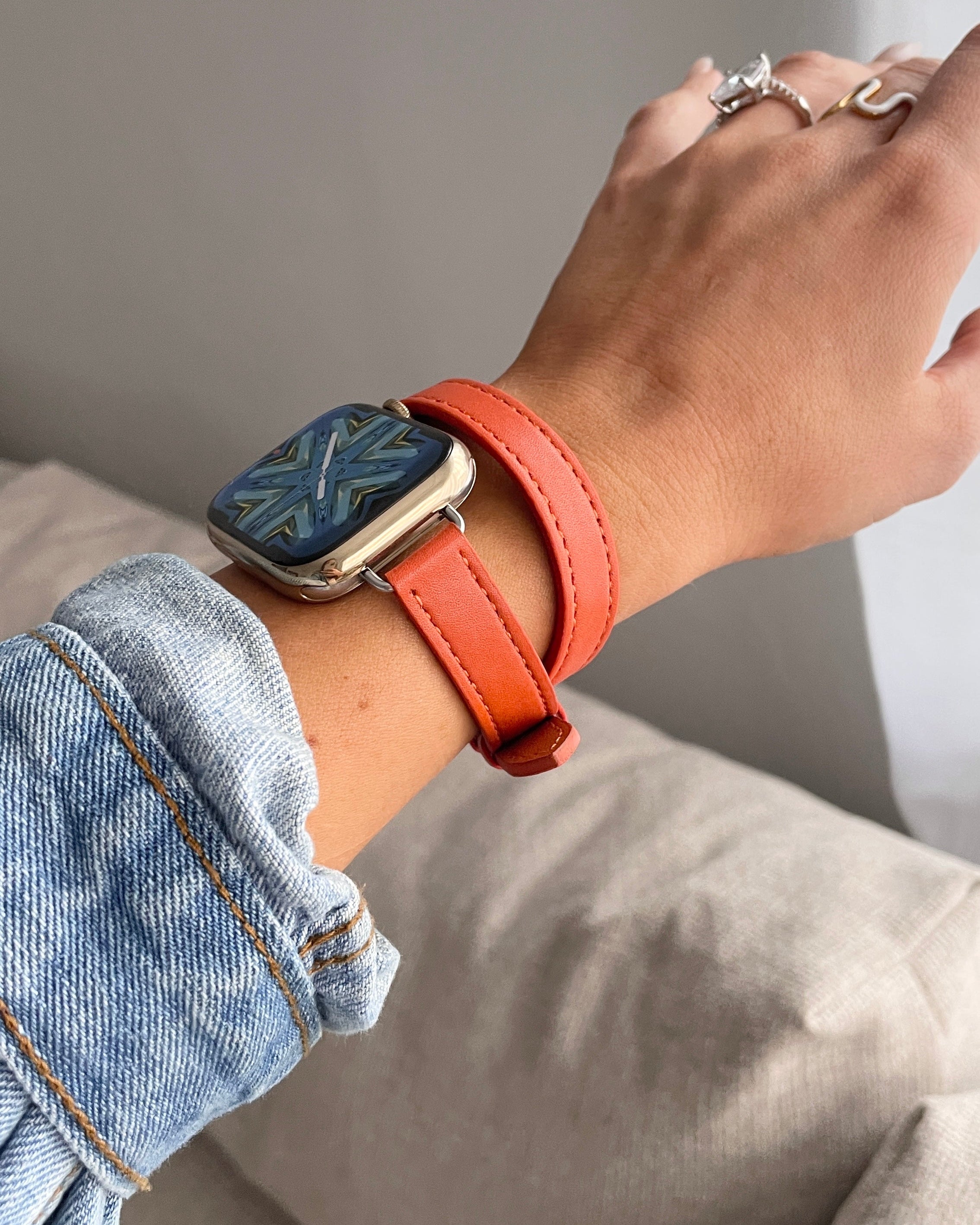 Person wearing a smartwatch with an orange leather strap on a neutral background