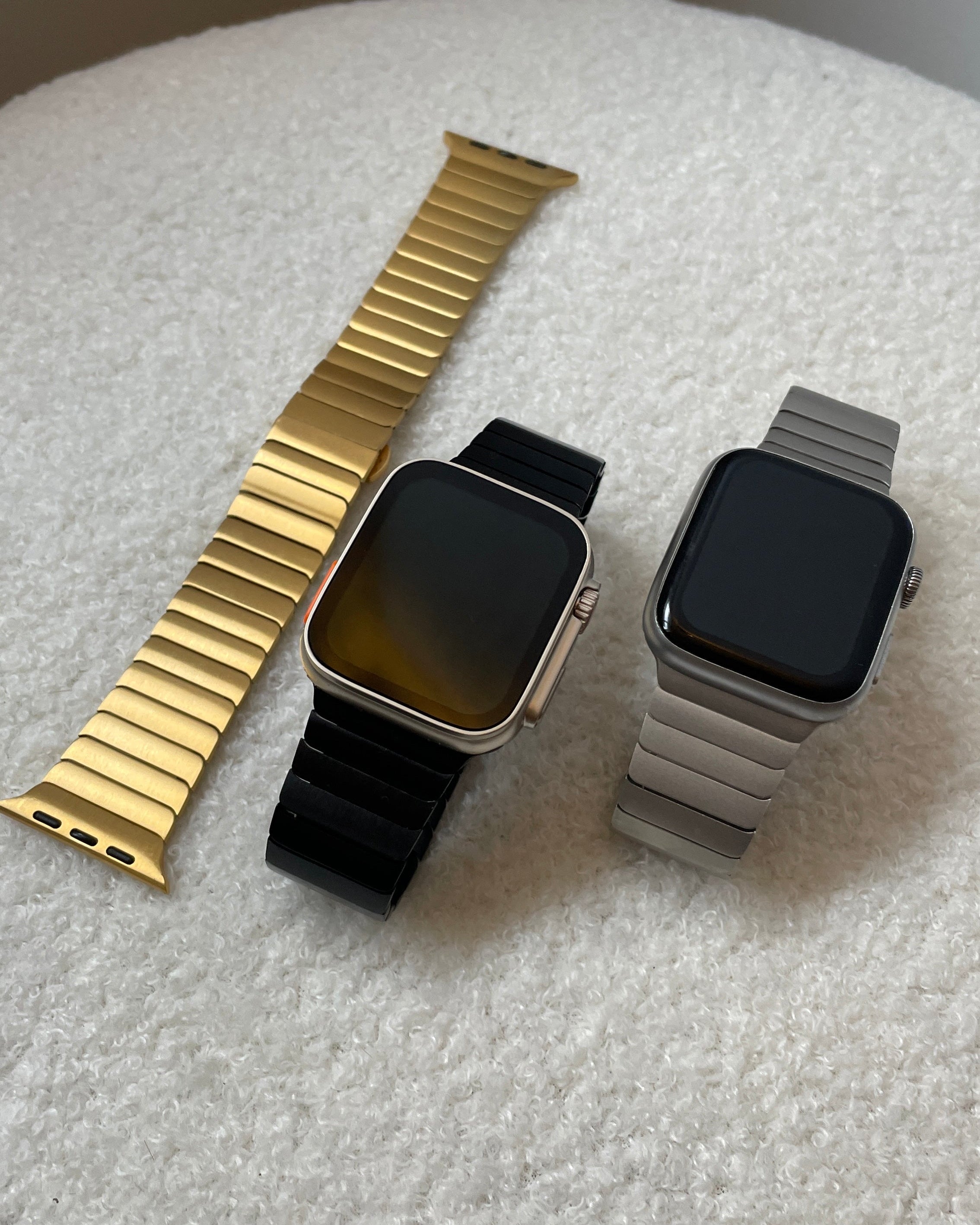 Three smartwatches with different colored bands on a textured surface