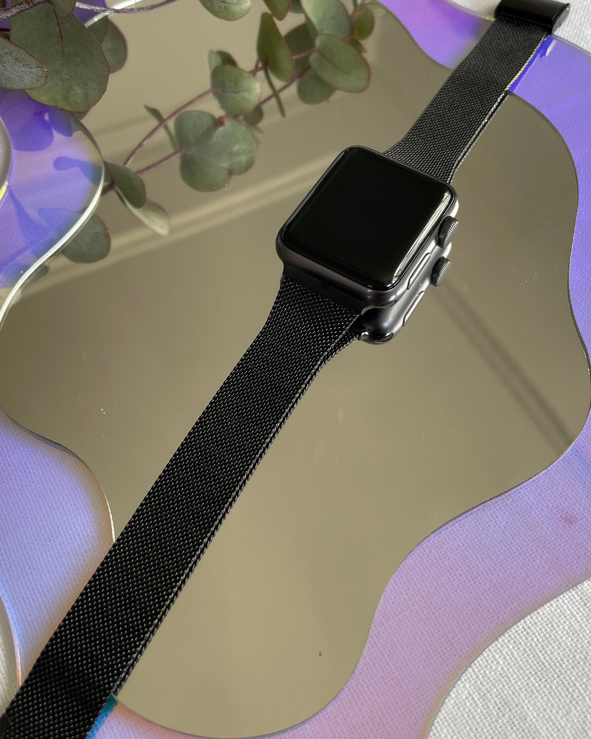 Smartwatch with a black band on a reflective surface with greenery in the background