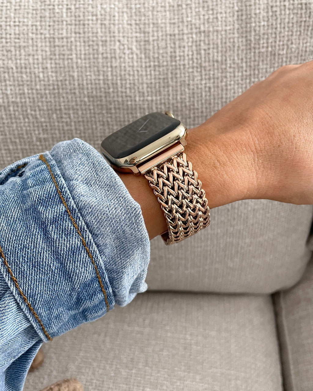 Person wearing a smartwatch with a braided brown band on a gray couch.