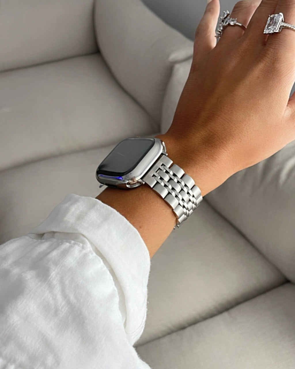 Hand wearing a silver watch on a light gray sofa