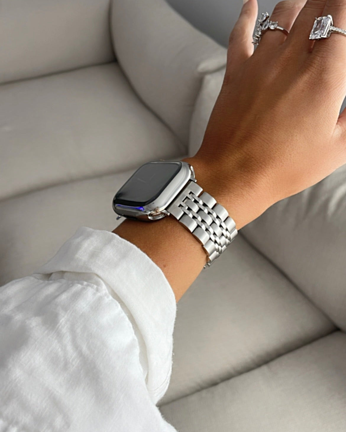 Hand wearing a silver watch on a light gray sofa