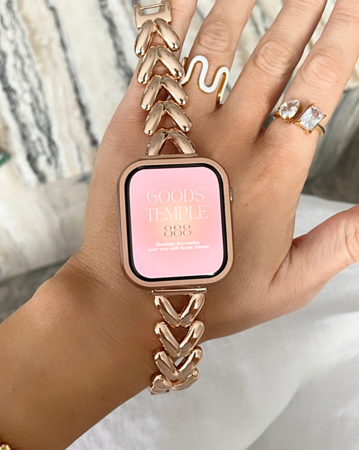 Hand wearing a rose gold smartwatch with a pink display on a neutral background
