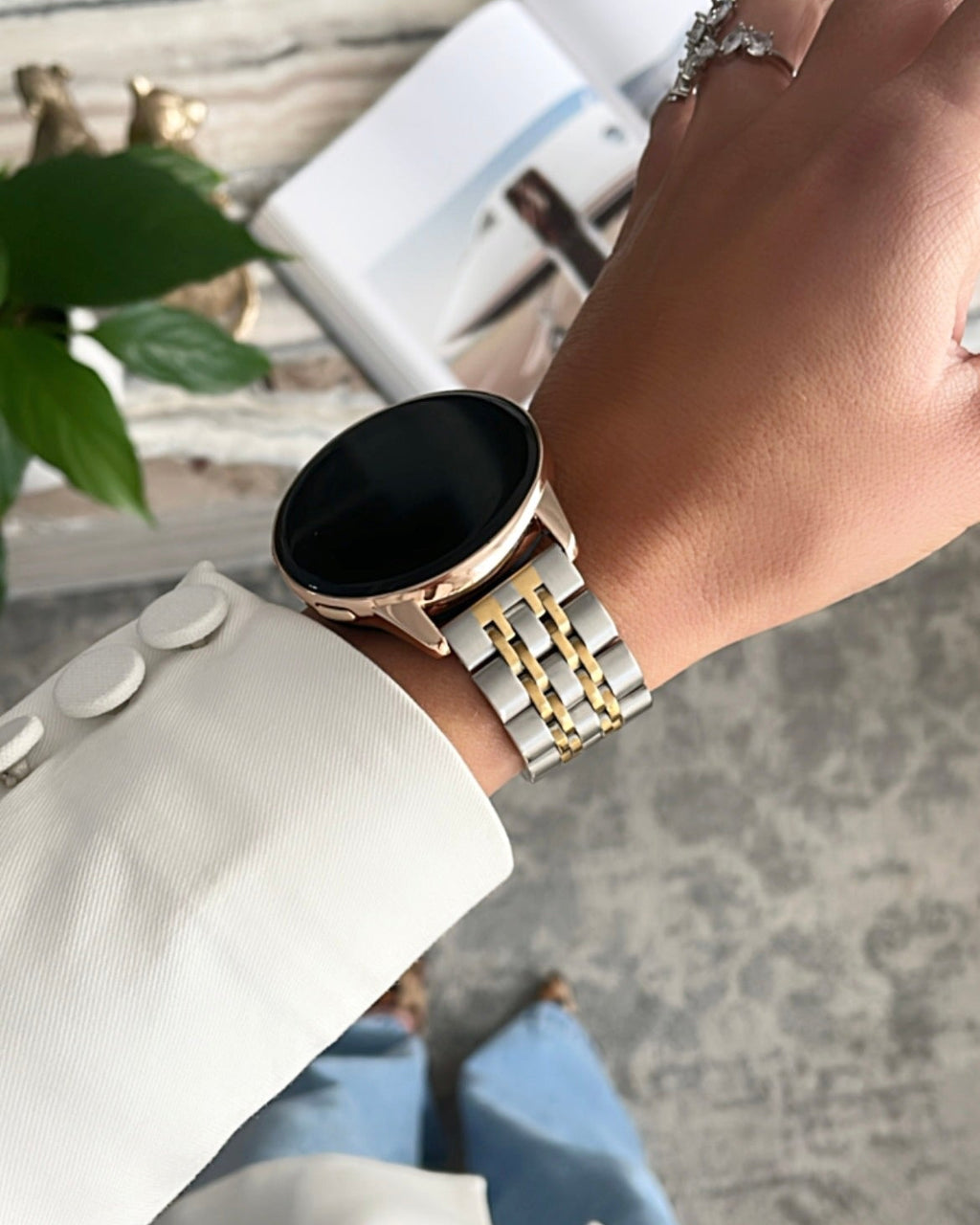 Hand wearing a smartwatch with a gold chain strap on a blurred background
