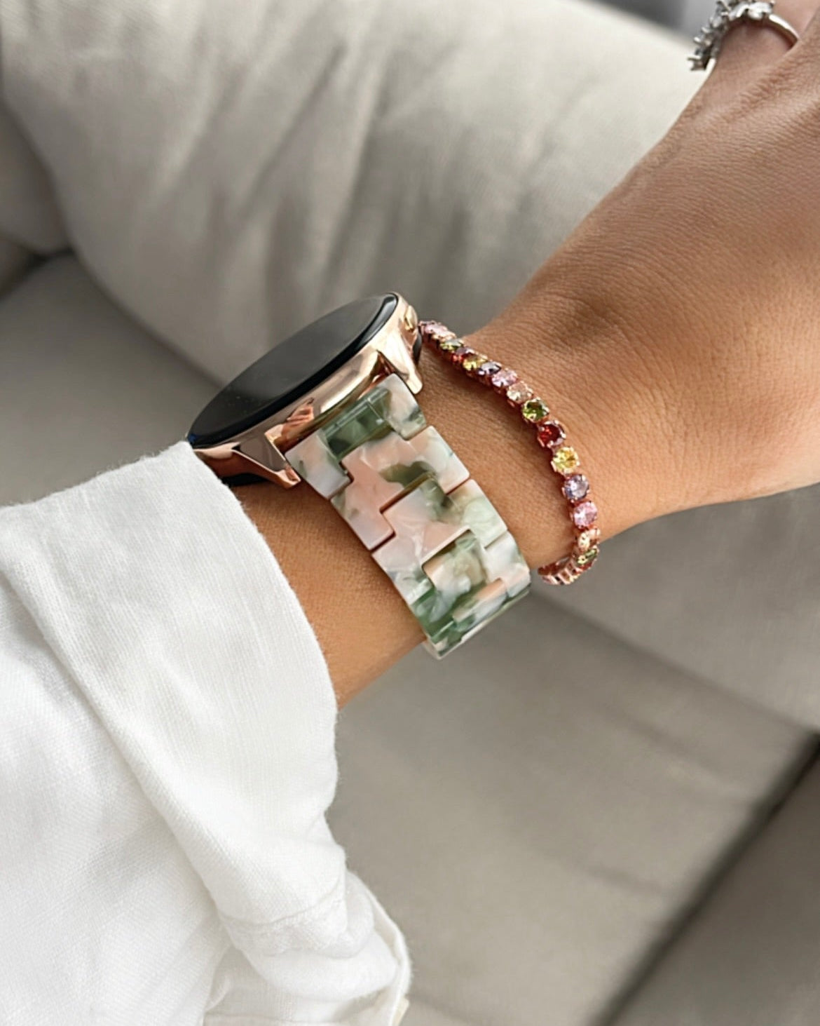Person wearing a floral smartwatch and colorful beaded bracelet on a neutral background