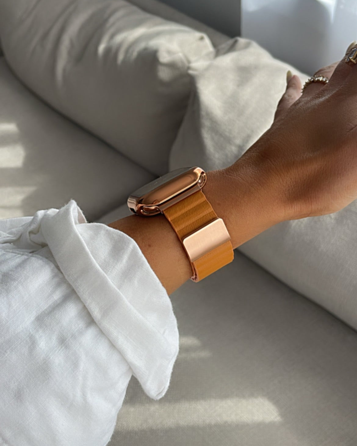 Person wearing a gold bracelet on a light-colored sofa with sunlight filtering through a window.