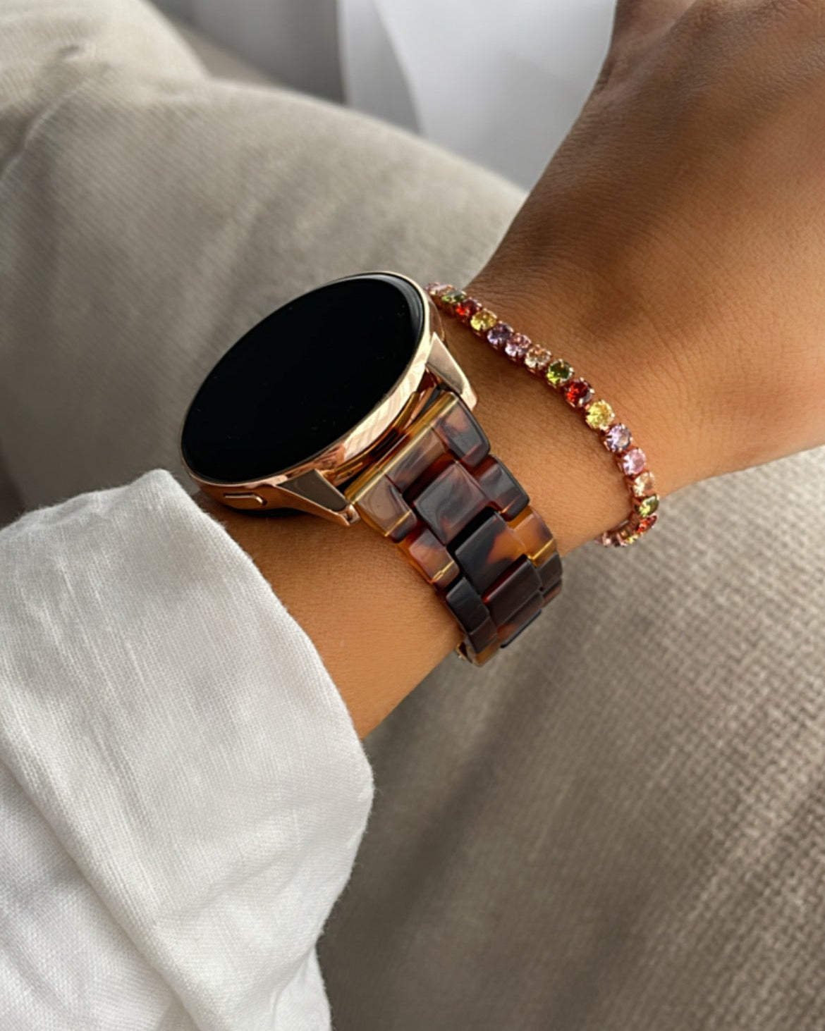 Smartwatch on a wrist with a colorful bracelet against a neutral background