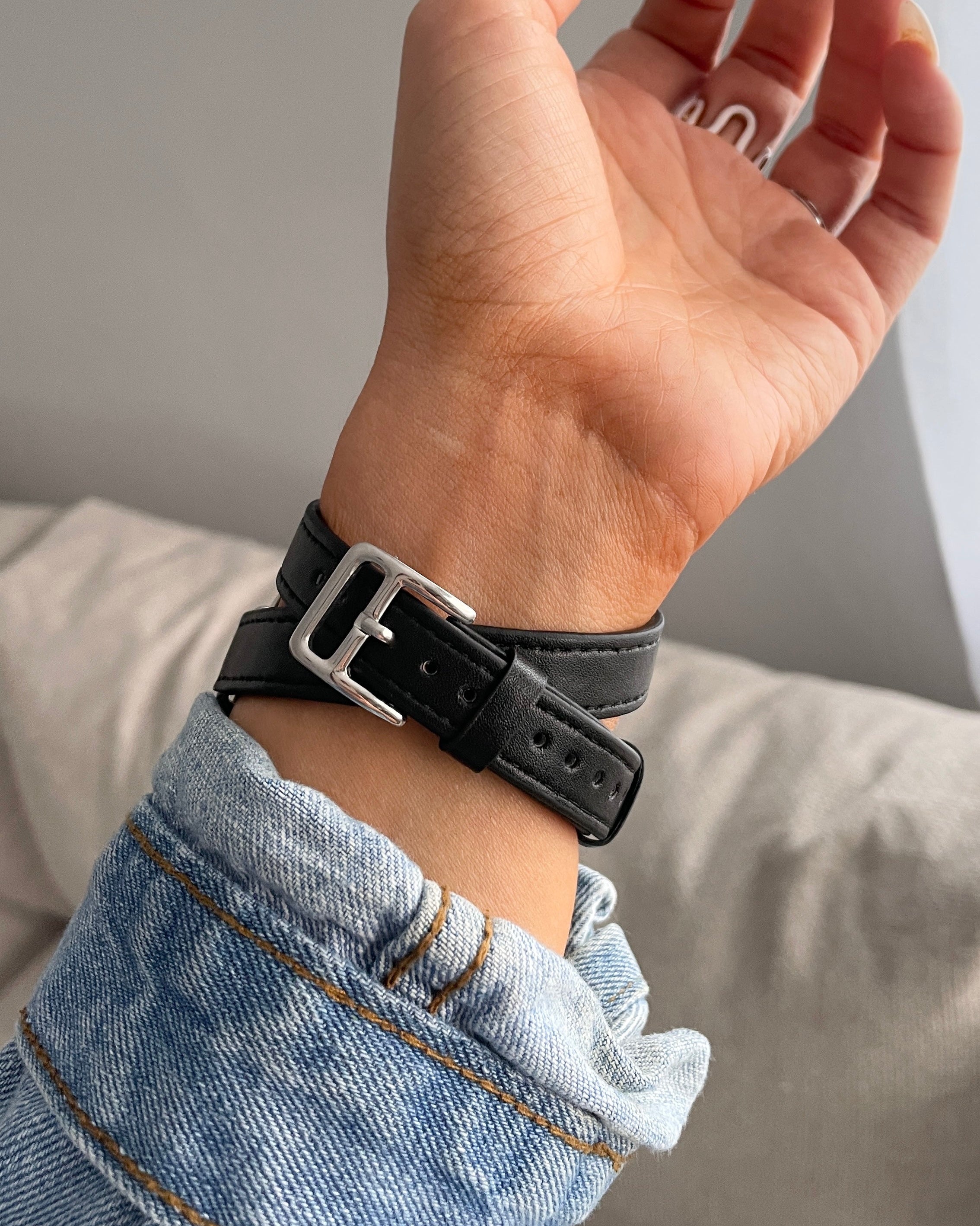 Hand wearing a black leather wristband with a silver buckle on a neutral background