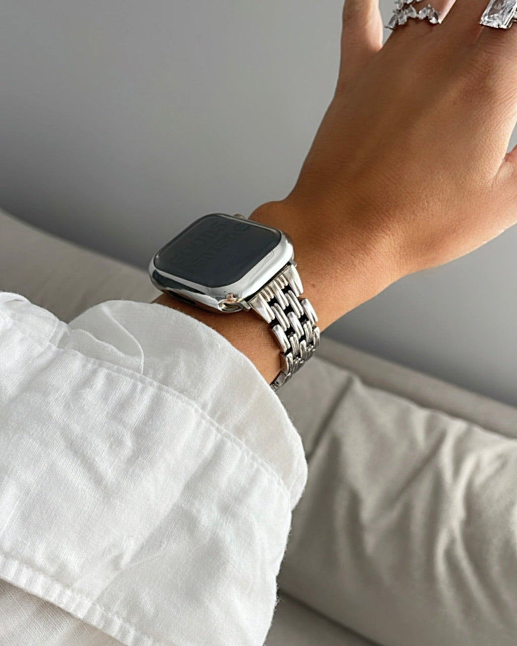 Hand wearing a smartwatch with a white shirt sleeve on a neutral background