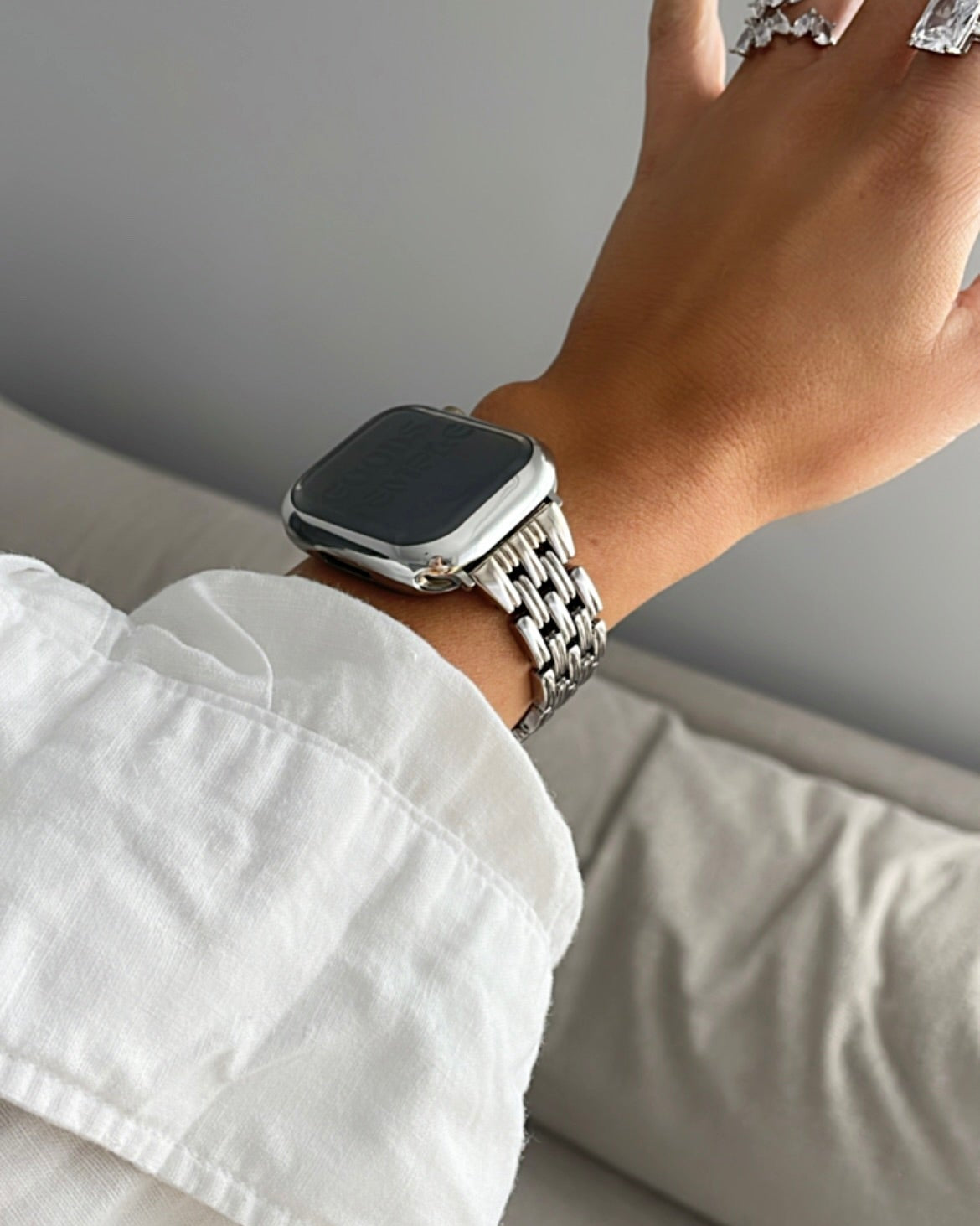 Hand wearing a smartwatch with a white shirt sleeve on a neutral background