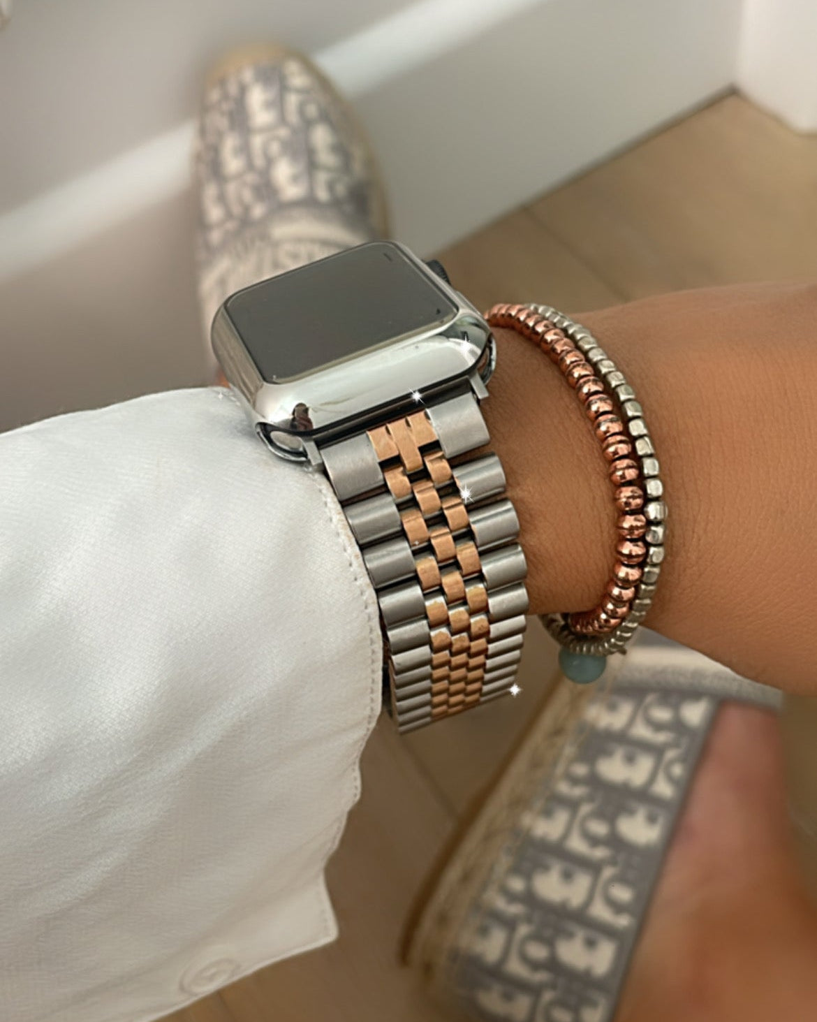 Close-up of a wrist wearing a silver smartwatch and multiple bracelets on a blurred background