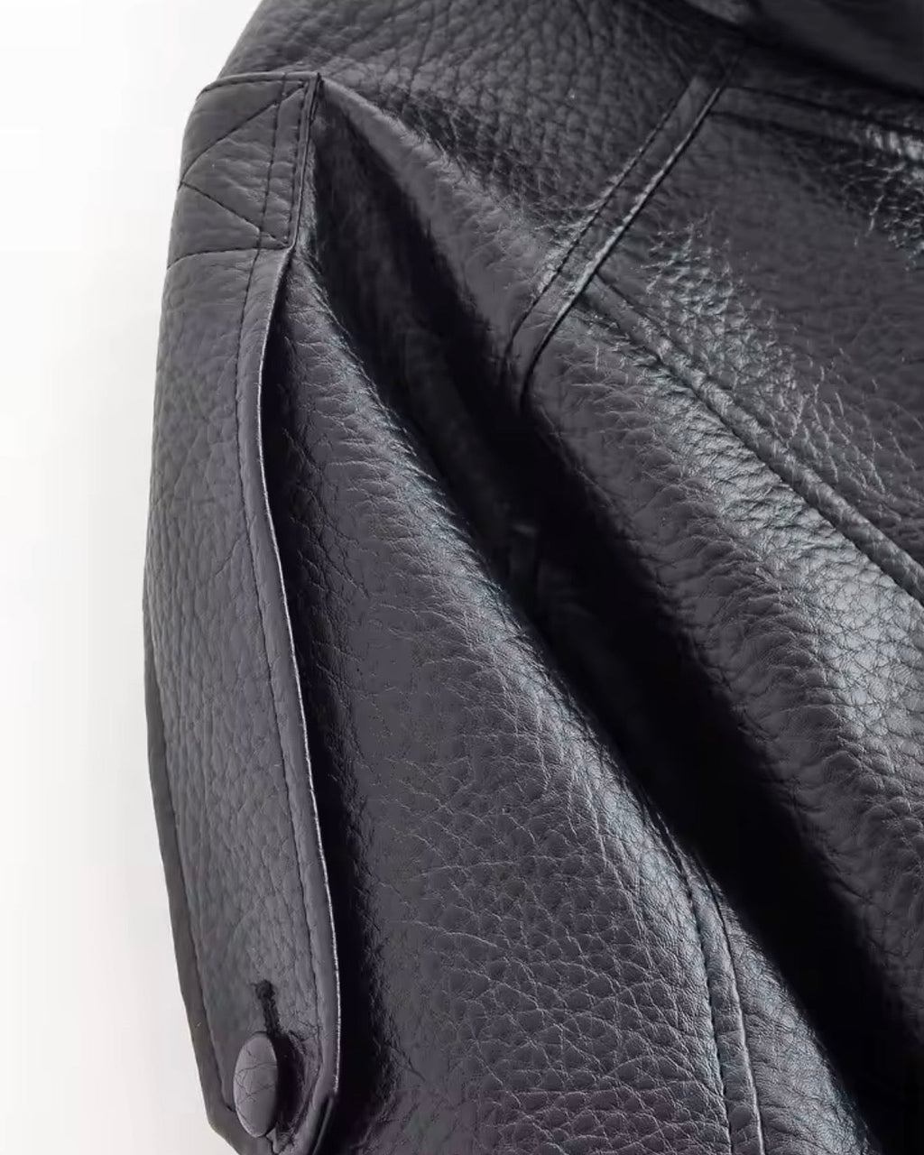 Close-up of a black leather jacket with a button on a white background