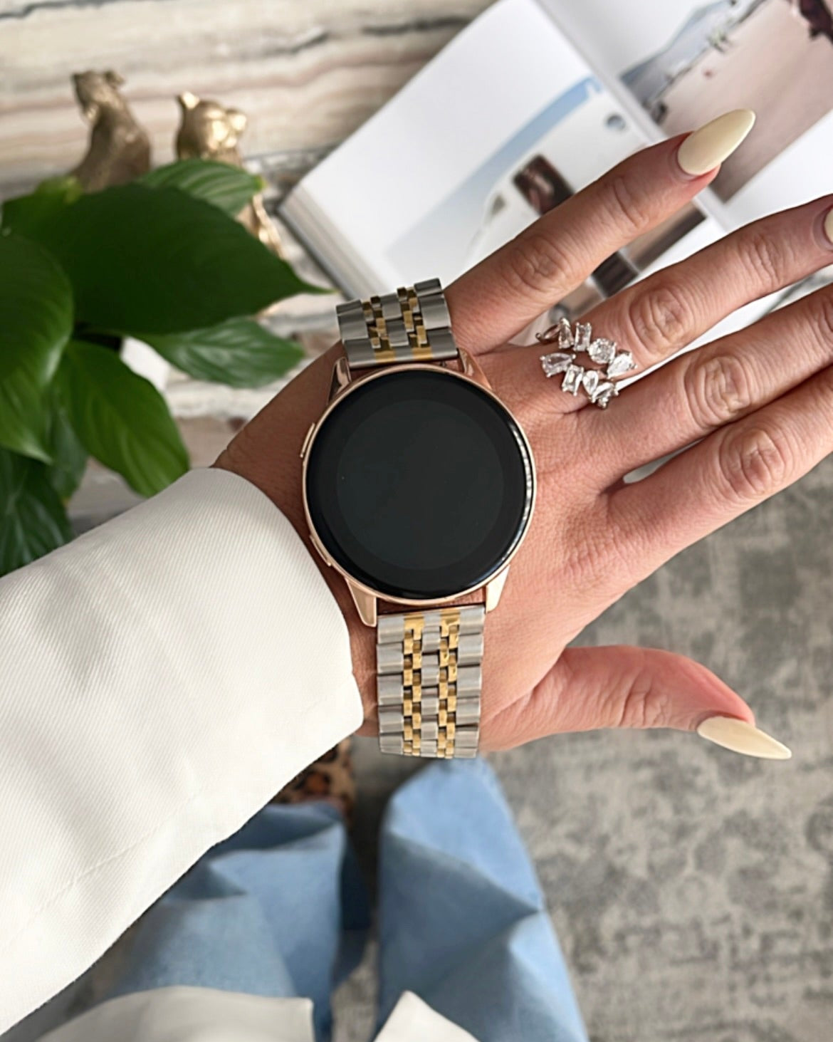Hand wearing a gold watch with a blurred indoor background