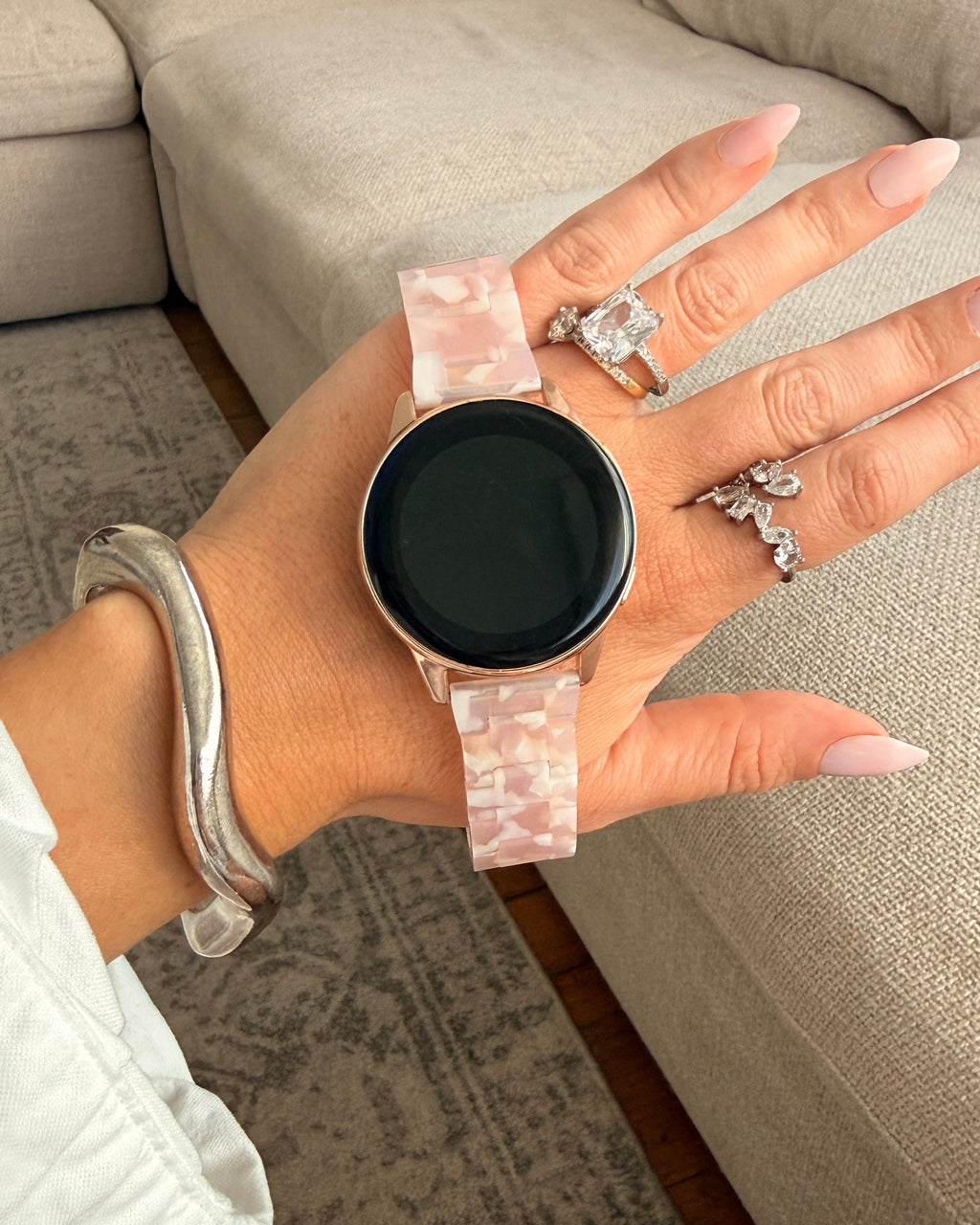 Hand holding a smartwatch with a pink strap in a living room setting
