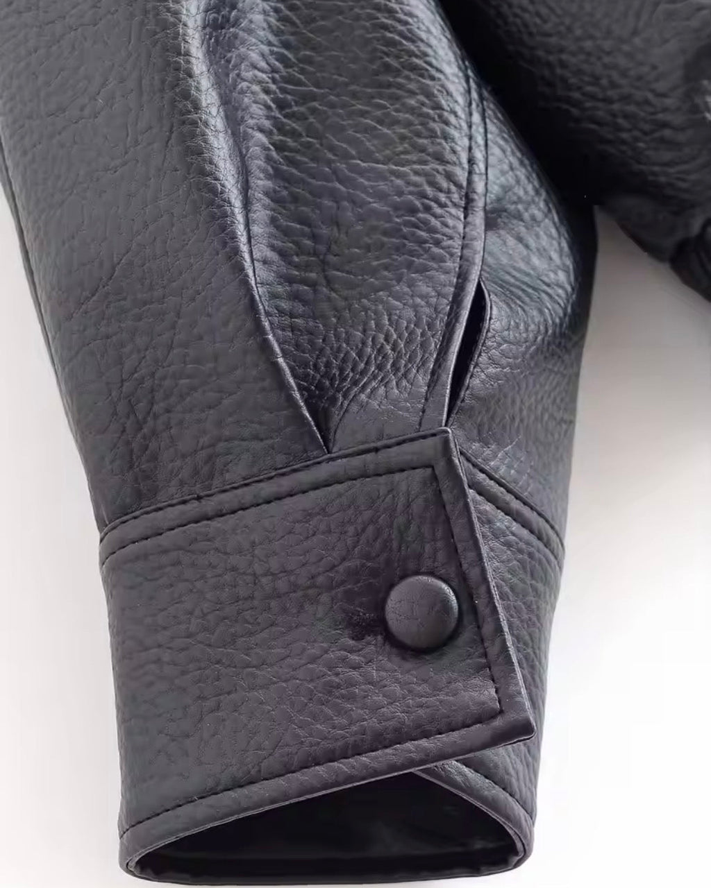 Close-up of a black leather glove with a button on a white background