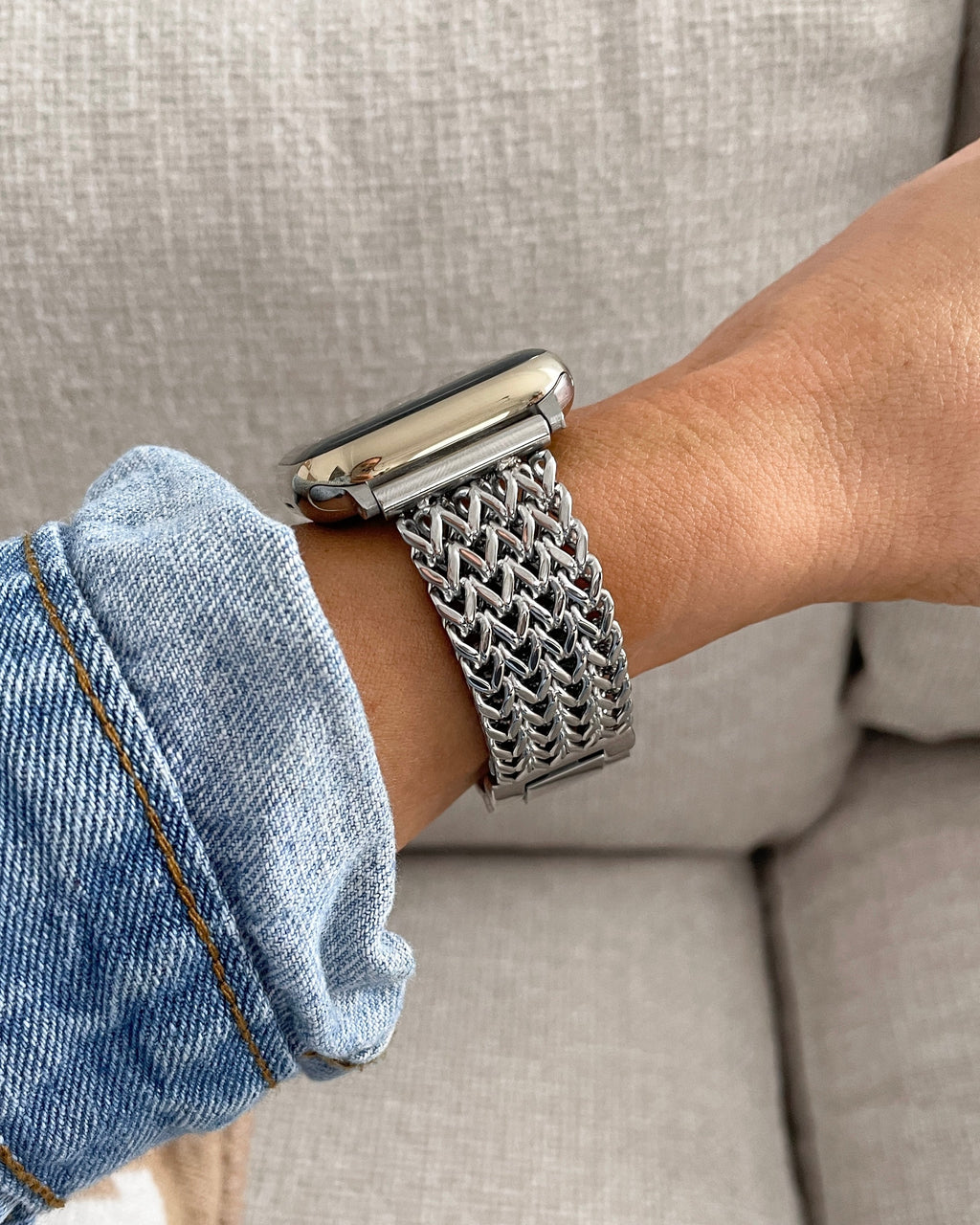 Person wearing a silver mesh watch on a beige couch