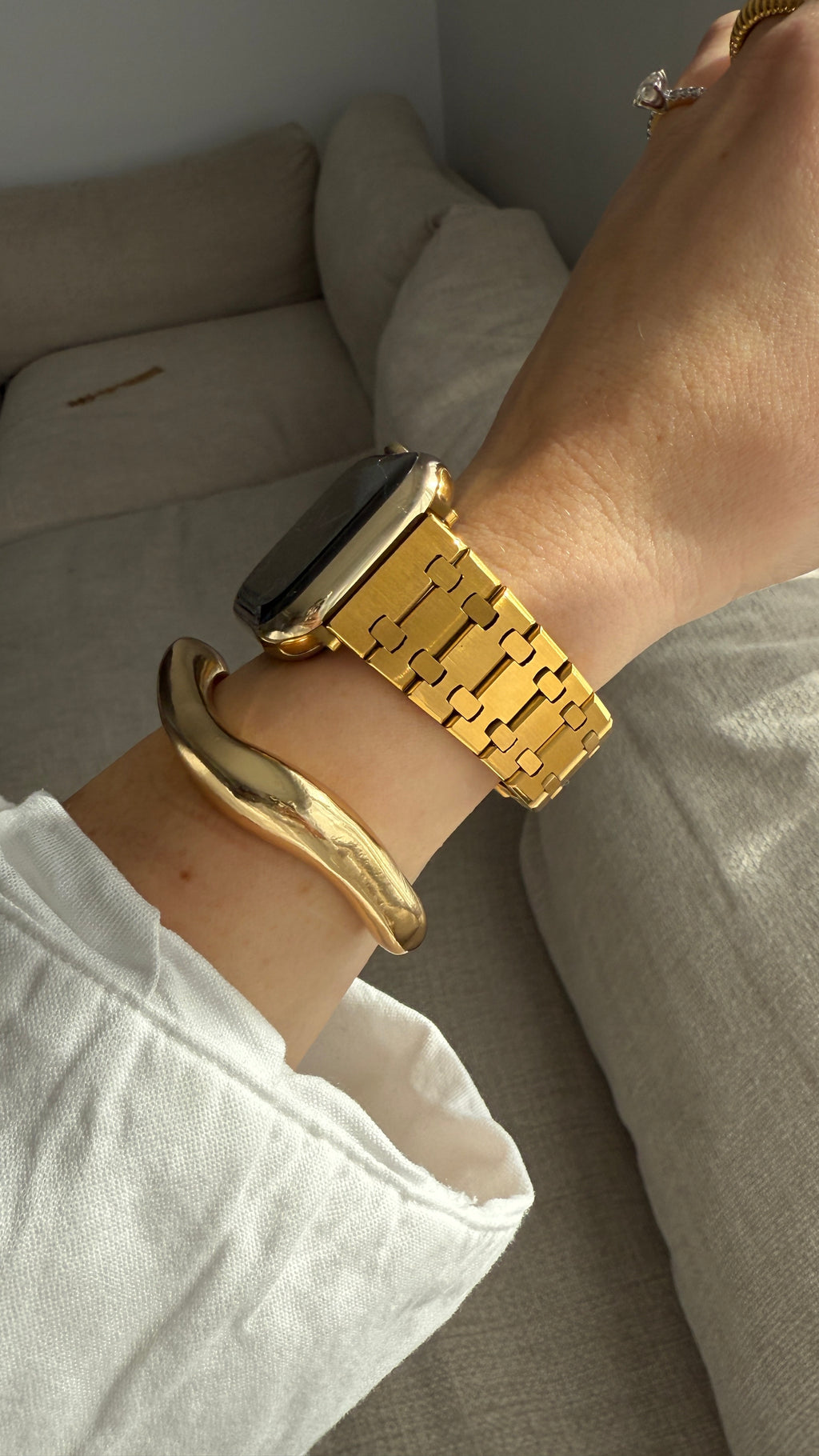 Gold watch and bracelet on a wrist with a neutral background