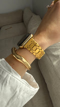 Gold watch and bracelet on a wrist with a neutral background