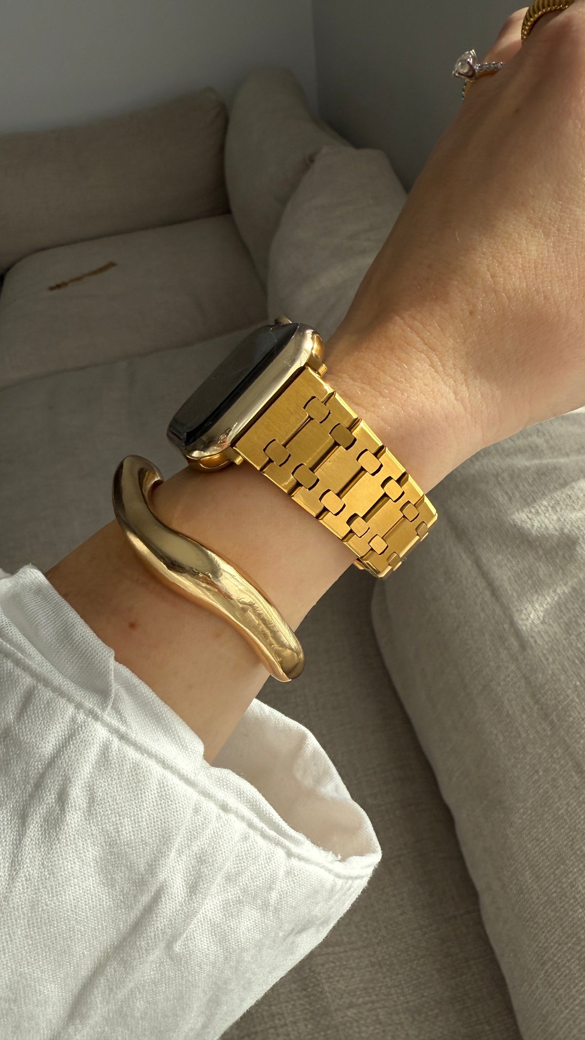 Gold watch and bracelet on a wrist with a neutral background