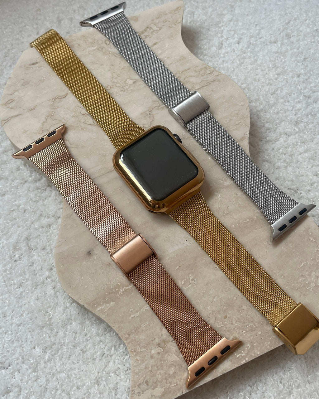 Set of Apple Watch bands in gold, silver, and rose gold on a stone surface