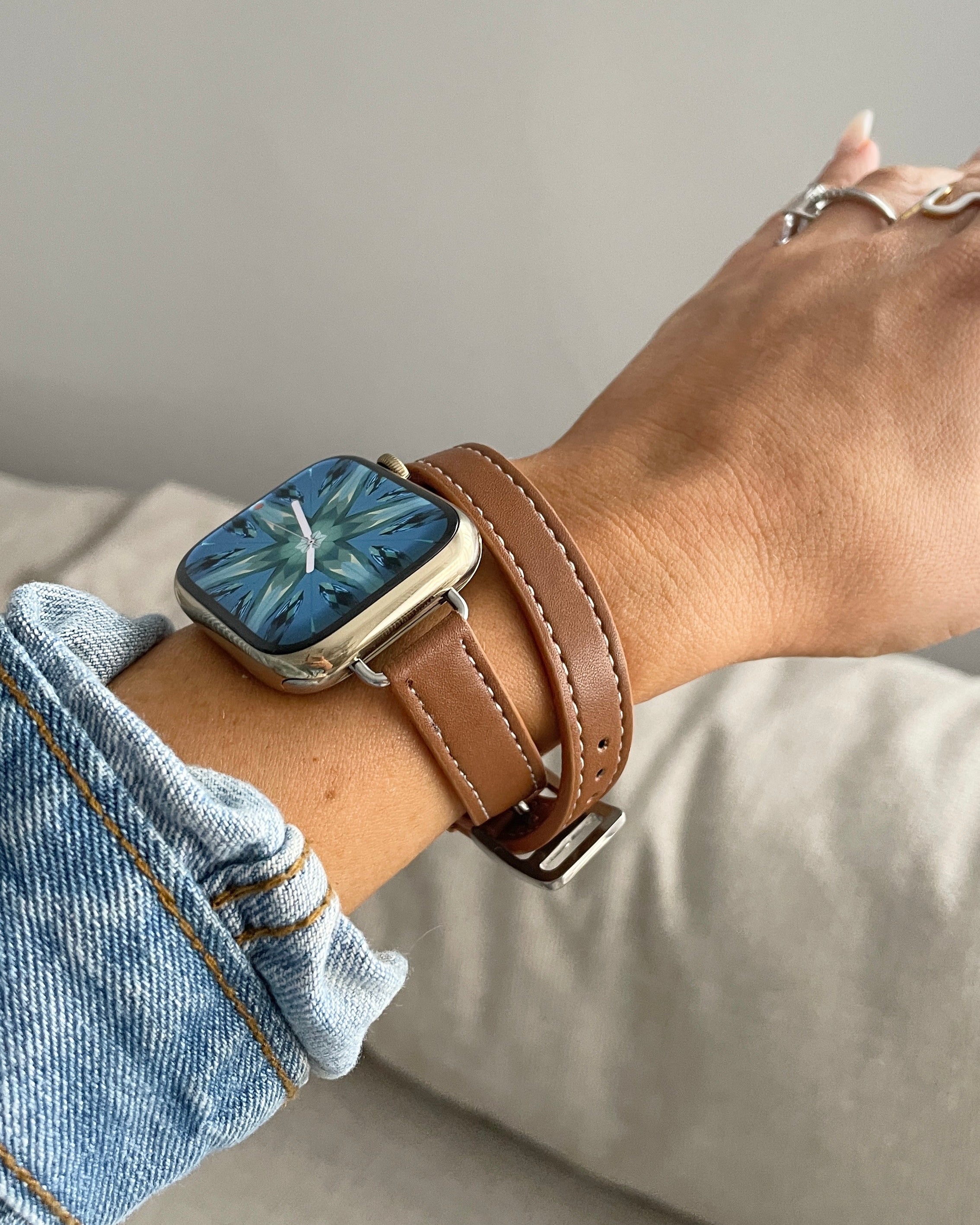 Person wearing a smartwatch with a brown leather strap on a neutral background