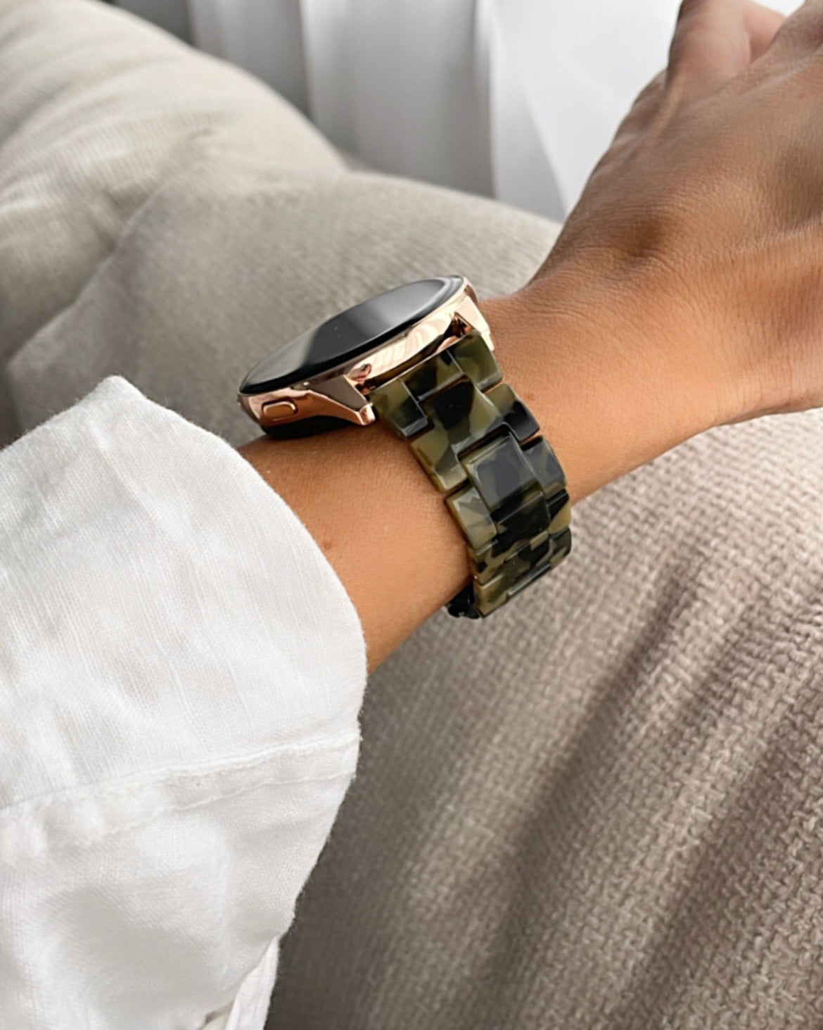Person wearing a smartwatch with a camouflage band on a neutral background