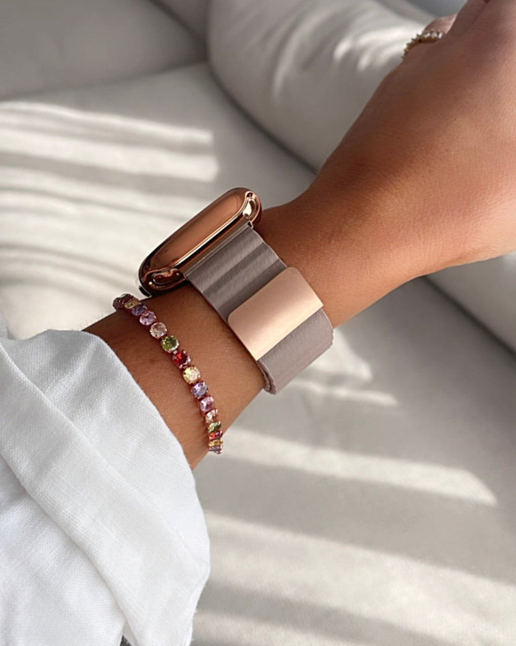 Close-up of a wrist wearing a smartwatch and bracelets on a light background